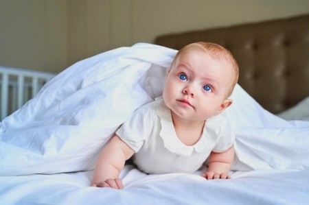 Un petit enfant aux yeux bleus se trouve sur lit