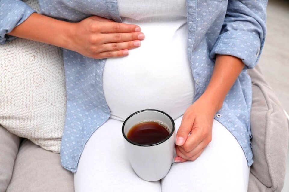 Femme enceinte boit du café avec une tasse
