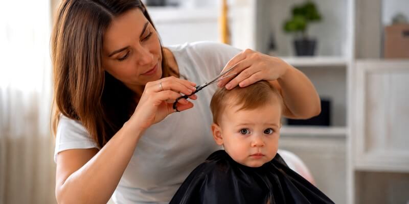 Jeune maman coupe les cheveux de son bébé